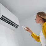 Woman holding remote control aimed at the air conditioner.