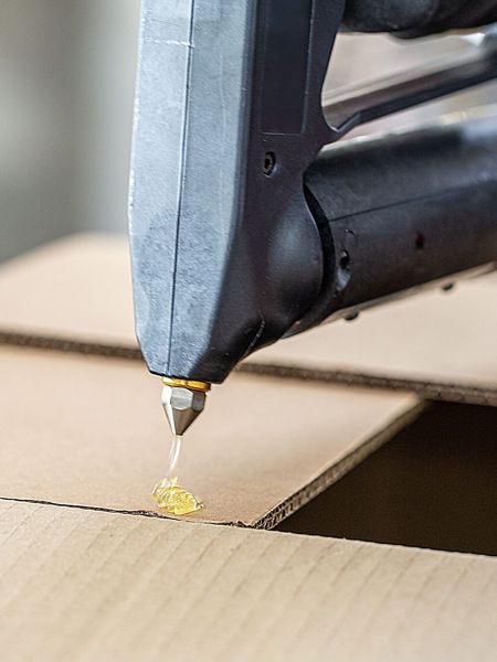 Handheld bulk hot melt sprayer applying hot melt adhesive to a cardboard carton