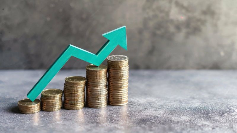Ascending stacks of coins with a green upward arrow representing financial growth, investment success, and economic improvement.