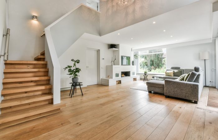 A cozy house interior with a wooden floor, large gray sofa, and stairs leading to the second floor